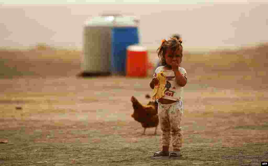 A displaced child who fled from the Islamic State (IS) group bastion of Raqqa stands outside as she eats a loaf of bread in a camp for displaced persons near the town of Al-Karamah, Syria. (AFP/Delil Souleiman)