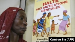 Женщина проходит мимо плаката, поддерживающего отмену женского обрезания