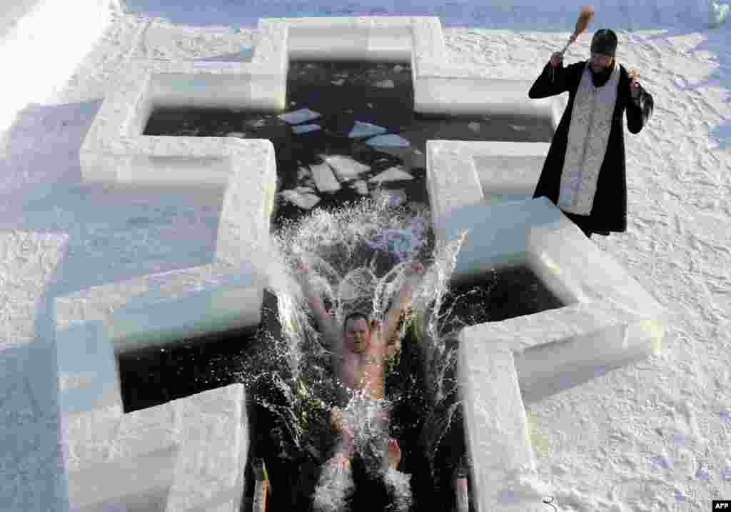 A plunge into near-freezing waters as an Orthodox priest blesses the bather on the eve of Epiphany in Pilnitsa, Belarus. (AFP/Viktor Drachev)