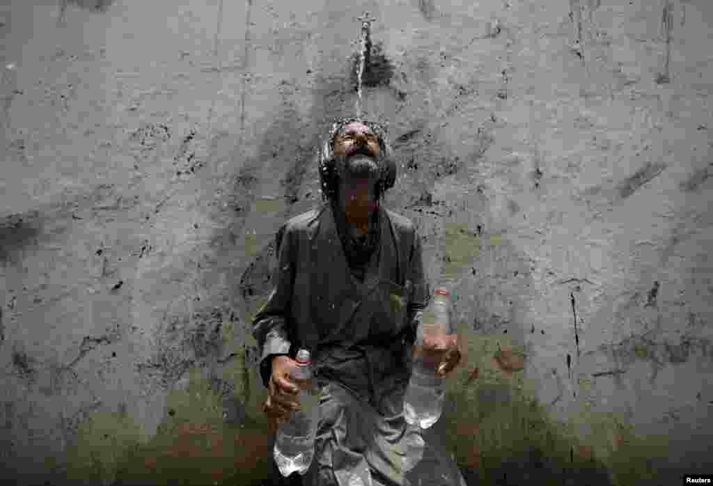 A Karachi man cools off under a public tap after filling bottles with water.