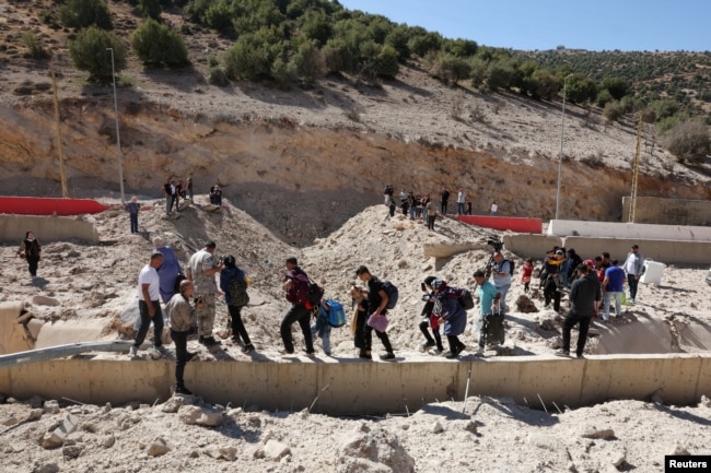 People carry their belongings while walking next to the rubble, after an Israeli strike, at the Masnaa border crossing.