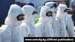 Men in protective masks and uniforms disinfect a street in Osh from the coronavirus on April 4.