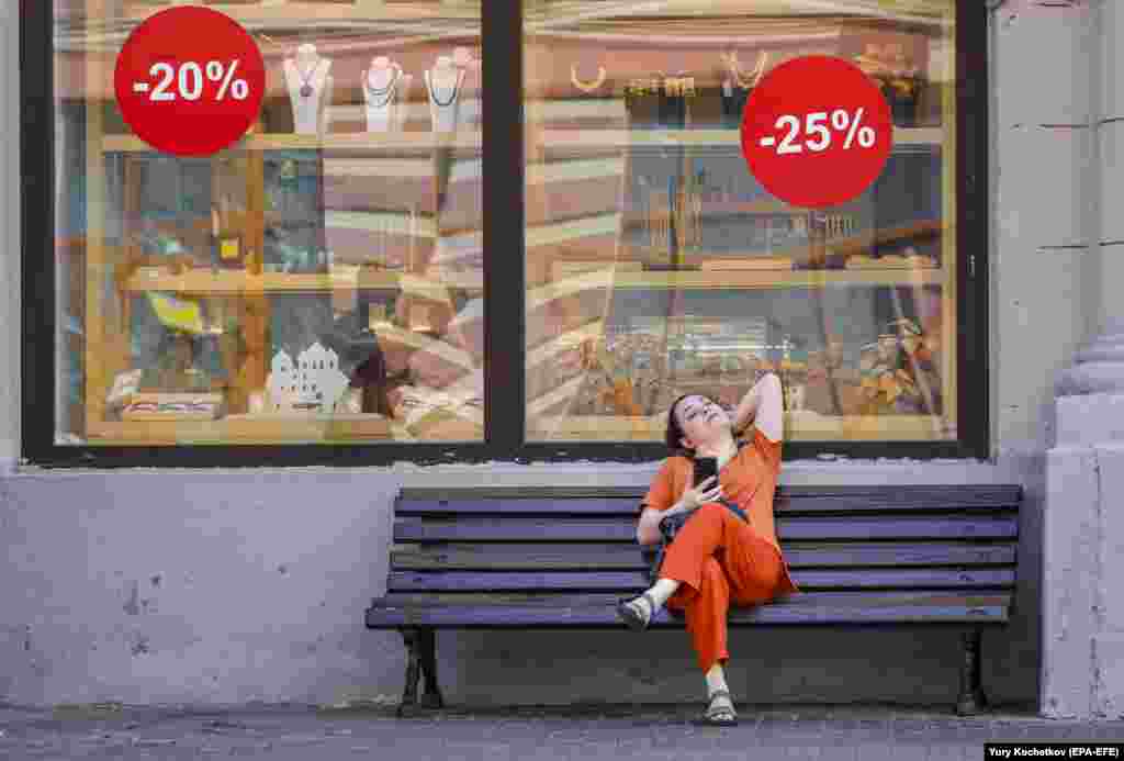 A woman sits on a bench in front of a shop in Moscow.