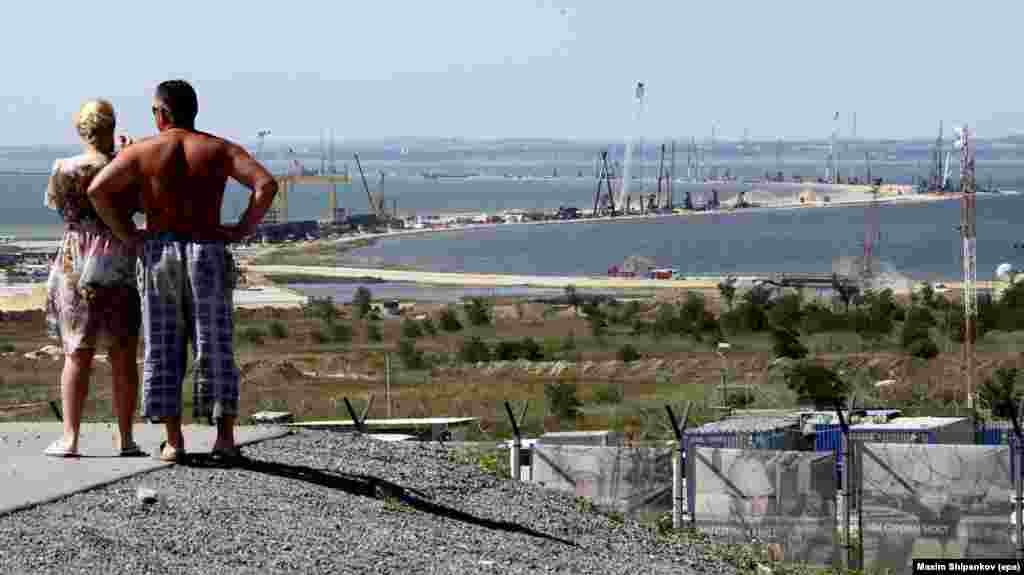 People near the Russian town of Taman look out in July 2016 over the construction of the Kerch bridge, snaking 19 kilometers toward Crimea. A crew of around 5,000 people are working around the clock on the project, which began in May 2015.&nbsp;