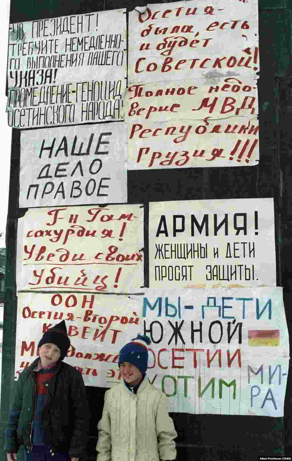 Gyerekek&nbsp;Chinvali&nbsp;utcáin 1991. január 1-jén. A hátuk mögött olvasható feliratokon ez áll: &quot;Oszétia mindig is szovjet volt és az is marad!&quot;. A grúzok közül sokan árulóknak tartották Oszétia lakóit, miközben az ország a Szovjetunióból való kiválásért harcolt. Mindeközben az oszét nép kirekesztve érezte magát azok miatt az új törvények miatt, amelyek a grúzt ismerték el egyetlen hivatalos nyelvként, és meggyengítették az oszét politikai képviseletet&nbsp;Tbilisziben.