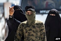 A security patrol member escorts reported wives of Islamic State (IS) fighters at the al-Hol camp in al-Hasakeh governorate in northeastern Syria, in 2019.