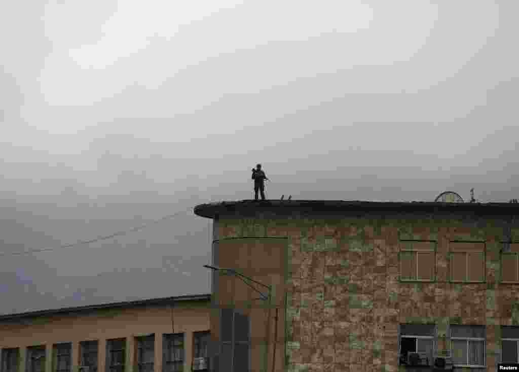 An Afghan security officer keeps watch atop a building near the presidential palace.