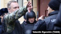 Oleg Sokolov (center), dressed in a bulky bullet-proof vest and helmet, was brought on November 15 to his apartment in St. Petersburg, where the head of his alleged victim was found.