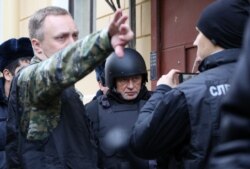 On November 15, Oleg Sokolov (center), dressed in bullet-proof clothing, was brought to his apartment in St. Petersburg, where his alleged victim's head had been found.