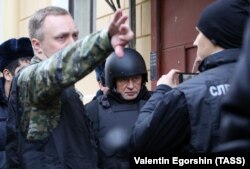 On November 15, Oleg Sokolov (center), dressed in bullet-proof clothing, was brought to his apartment in St. Petersburg, where his alleged victim's head had been found.