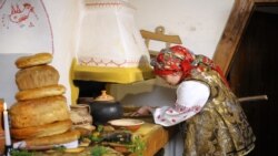 Жінка в українському традиційному вбранні ставить казан у піч для приготування куті – різдвяної страви