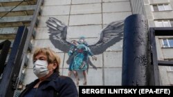 A woman walks in front of graffiti showing a doctor trying to help a patient with COVID-19, in the Moscow region.