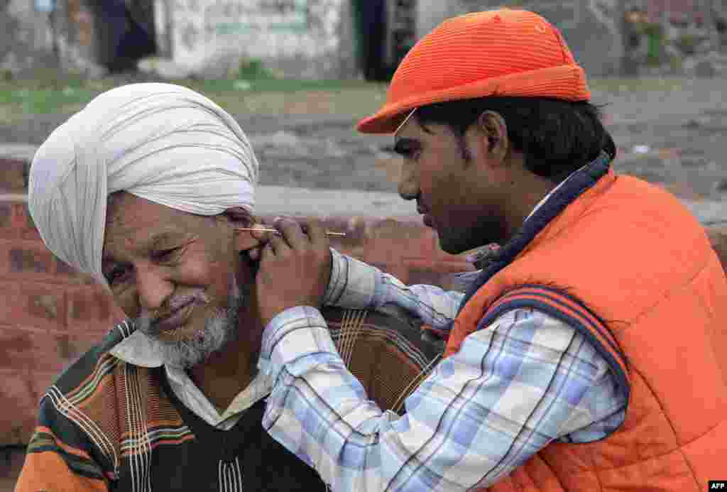 Indian ear cleaner Sunil Kumar (right) tends to a customer on the road in Amritsar. Ear cleaners, or kaan saaf wallahs as they are locally known, are a common sight in Indian cities where customers pay to have wax and dirt scraped from inside their ears. (AFP/Narinder Nanu)
