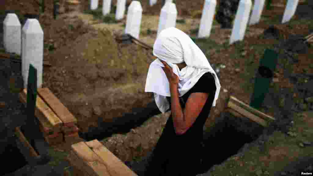 A woman cries near a new open grave with the coffin of her late relative&#39;s remains, prepared for burial on July 11.