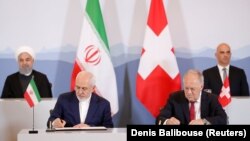 Swiss President Alain Berset (top right) and Iranian President Hassan Rohani (top left) look on as Johann Schneider-Ammann, head of the Federal Department of Economic Affairs, Education and Research (right) and Iran's Foreign Minister Mohammad Javad Zarif sign documents in Bern on July 3.