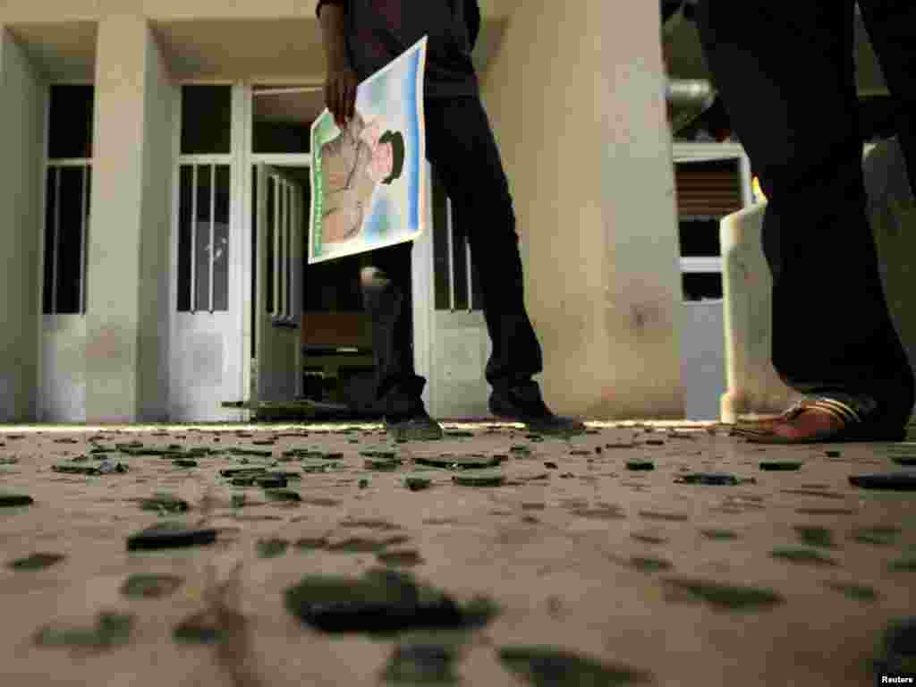 A student carries a picture of Libyan leader Muammar Qaddafi as she stands near pieces of glass from broken windows, which the government said was caused by a Western air strike, at Al-Fatah University in Tripoli on April 14. Photo by Zohra Bensemra for Reuters