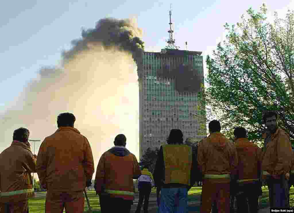 Street cleaners watch the headquarters of Yugoslav President Slobodan Milosevic's ruling Socialist Party burn after an early morning NATO air attack on Belgrade in 1999.