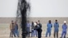 Iraqi workers stand near a pipeline as it ejects oil at Al Tuba oil field in southern Iraq