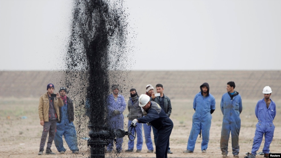 Iraqi workers stand near a pipeline as it ejects oil at Al Tuba oil field in southern Iraq