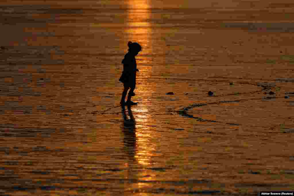 Дзяўчына ходзіць па пляжы падчас захаду сонца ў Карачы, Пакістан