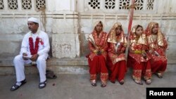 FILE: A groom (L) and four brides sit outside the venue of their weddings as they have arrived late to a mass Muslim marriage ceremony in the western city of Ahmedabad.