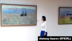 Суретші Молдахмет Кенбаевтың көрмеге қойылған "Әңгіме үстінде" картинасының жанынан өтіп бара жатқан адам. Алматы, 7 тамыз 2015 жыл.