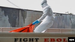В Либерии один из медицинских сотрудников в специальном костюме переносит тело умершего от Эболы 