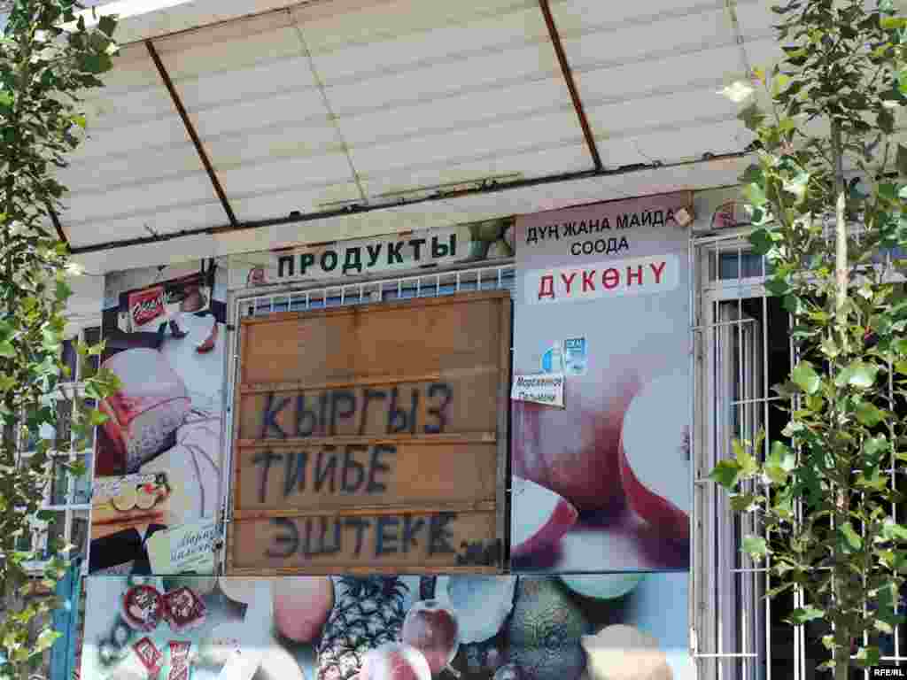  Кыргызский магазинчик остался нетронутым на фоне сожженных зданий в центре Оша. 18 июня 2010 года.