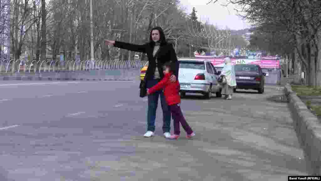 Waving for a taxi with her child on a street in Dushanbe