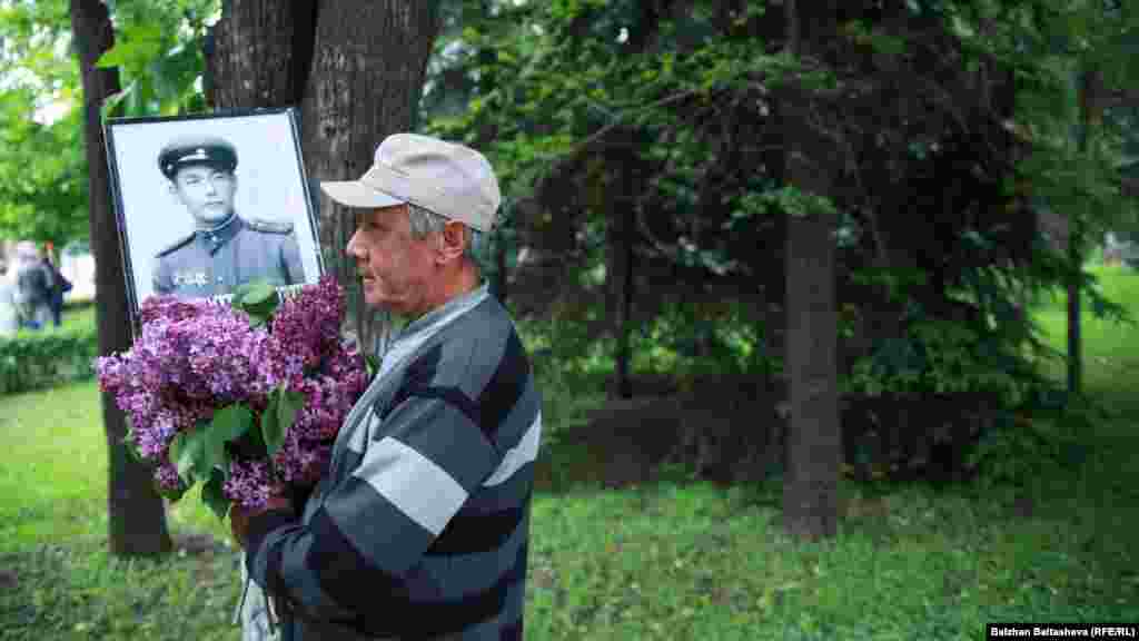 Мужчина держит цветы и портрет участника войны. Шествие &laquo;Бессмертный полк&raquo; в Алматы.&nbsp;