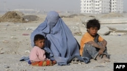A burqa-clad woman begs with her children near a newly constructed building in Kabul.