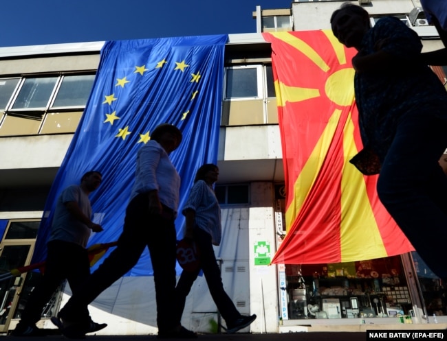 Cetățenii trec pe lângă steagurile UE și ale Macedoniei de Nord (dreapta), în timpul marșului pentru Macedonia Europeană în centrul capitalei Skopje, 16 septembrie 2018. EPA-EFE/NAKE BATEV