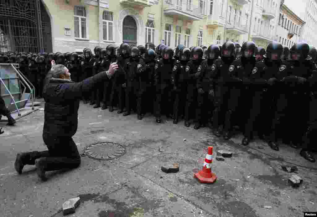 A Ukrainian man kneels down while riot police stand guard near the presidential administration building during a rally held by supporters of EU integration in Kyiv. (Reuters/Gleb Garanich)