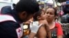 Мексиканский работник Красного Креста осматривает ребенка на руках женщины из Гондураса. 21 октября 2018