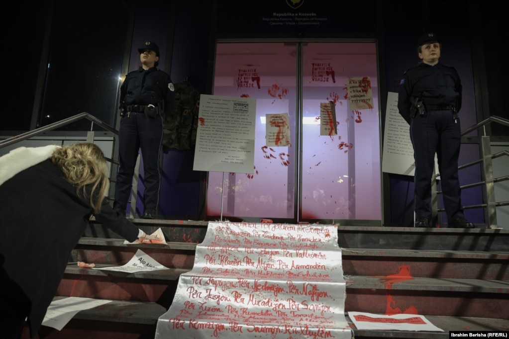 Dy police qëndrojnë roje teksa protestuesit ngjyrosin me bojë të kuqe portën e ndërtesës së Qeverisë dhe vendosin kopje të printuara të letrës që Arlinda Zekaj ua kishte dërguar organeve të drejtësisë për ta shqyrtuar rastin e saj.