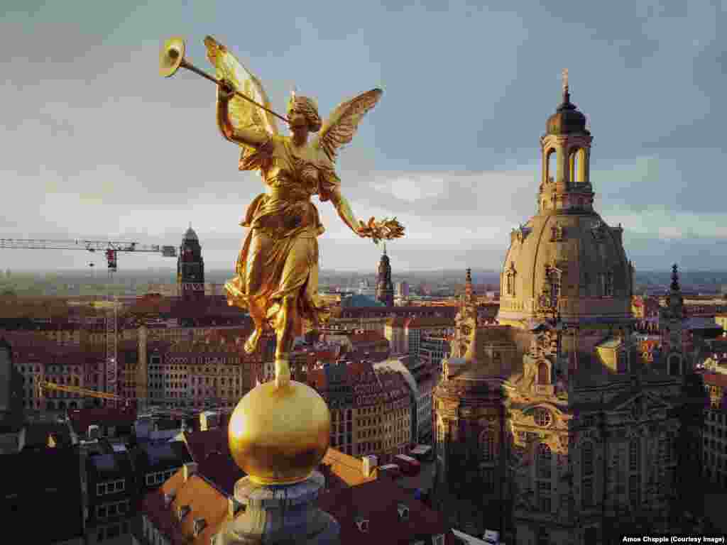 The golden sculpture of Pheme, the personification of fame and renown in Greek mythology, on the roof of the Dresden University of Visual Arts in Dresden, Germany, with the rebuilt Frauenkirche, which was destroyed in World War II bombing, in the background. (RFE/RL/Amos Chapple)