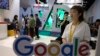 Visitors talk to staff members at a Google stand during the Global Mobile Internet Conference (GMIC) in Beijing, China, Friday, April 28, 2017.