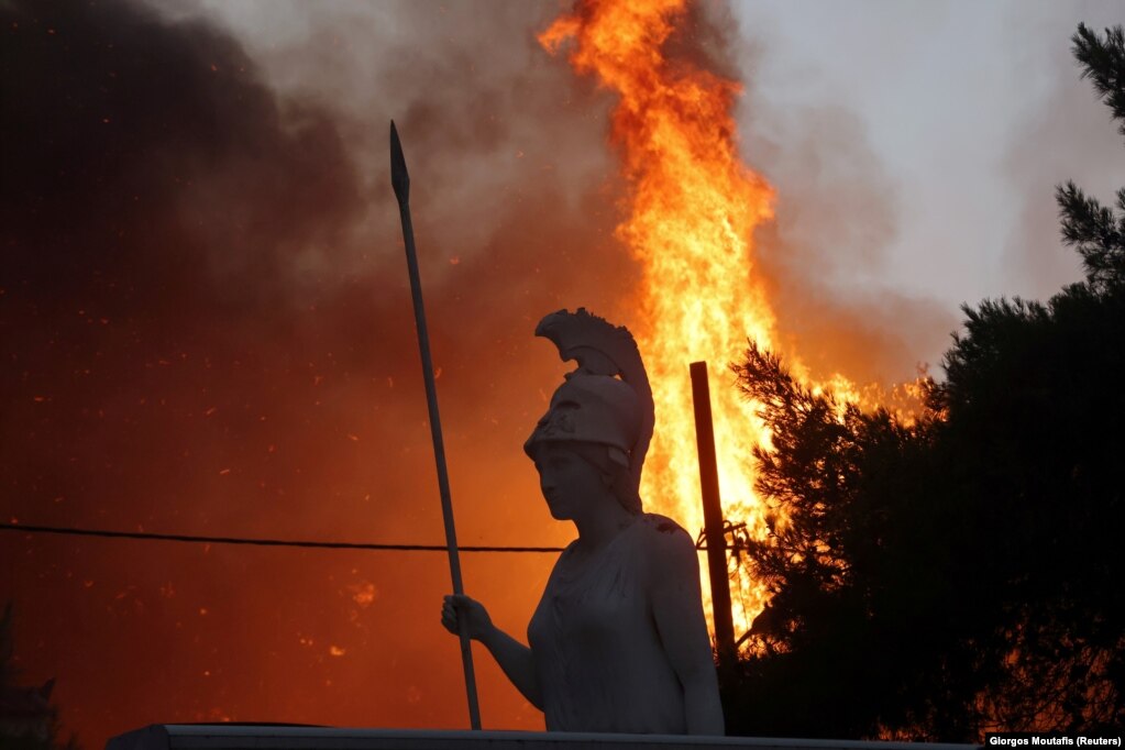 Pamje që shfaq një statujë të perendeshës Athena, teksa flakët e një zjarri të egër shkretonin periferinë e Athinës, në Greqi. (3 gusht)
