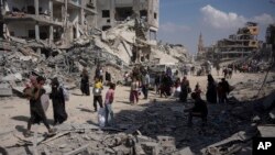 Palestinezët duke kaluar pranë ndërtesave të shkatërruara në Han Junis të Rripit të Gazës më 8 prill 2024. 