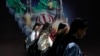 Iranian women without a mandatory head scarf, or hijab, walk past a banner in Tehran in April. 