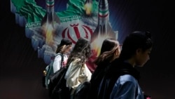 Iranian women without a mandatory head scarf, or hijab, walk past a banner in Tehran in April. 