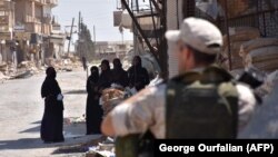 SYRIA -- A Russian military policeman stands guard as displaced Syrian women who are staying at a temporary shelter in Jibrin, on the outskirts of Aleppo, gather before being transported to areas currently controlled by the Syrian regime in eastern Aleppo