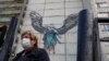 A woman walks in front of graffiti showing a doctor trying to help a patient with COVID-19, in the Moscow region.