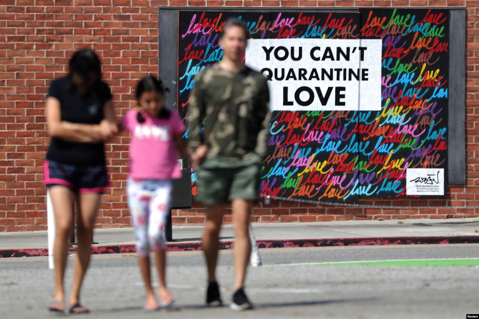 Tre persona ecin afër një murali në të cilin shkruan “Dashurinë nuk e fusni dot në karantinë”