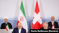 Swiss President Alain Berset and Iranian President Hassan Rohani look on as Johann Schneider-Ammann, Head of the Federal Department of Economic Affairs, Education and research and Iran's Foreign Minister Mohammad Javad Zarif sign documents 