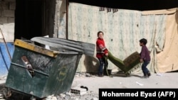 Children carry a chair in the street as people gather belongings in preparation for evacuation from eastern Ghouta.