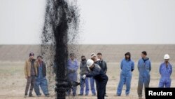 Iraq -- Iraqi workers stand near a pipeline as it ejects oil at Al Tuba oil field in Basra, February 19, 2015