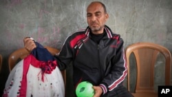 یک پدر فلسطینی و لباس دختر چهارساله‌اش مَسا که در دیرالبلح در نوار غزه کشته شد