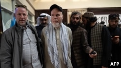 Talibanii îl escortează pe Dennis Coyle (în centru) către un avion charter la aeroportul din Kabul, pe 24 martie 2026, după ce l-au eliberat, după mai bine de un an de detenție.