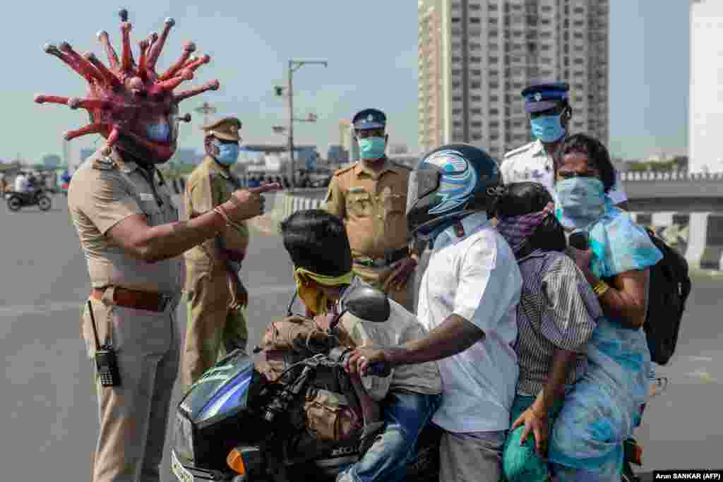 Inspectorul de poliție Rajesh Babu poartă o cască în formă de coronavirus în timp ce vorbește cu o familie pe motocicletă la un punct de control din Chennai, India, în timpul carantinei impuse de guvern.